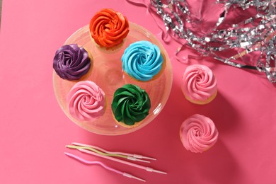 Photo of Delicious cupcakes with bright cream, candles and confetti on pink background, flat lay