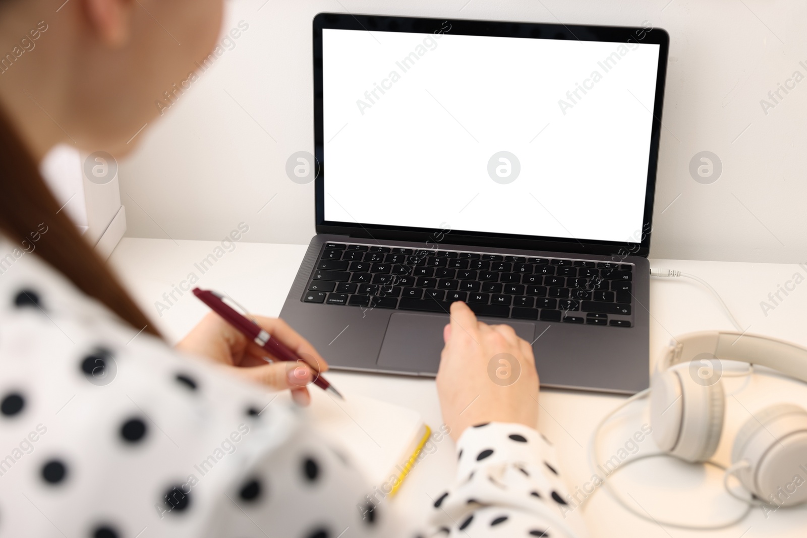 Photo of E-learning. Woman taking notes during online lesson at table indoors, closeup