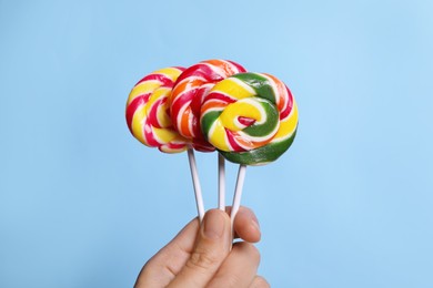 Woman holding bright tasty lollipops on light blue background, closeup