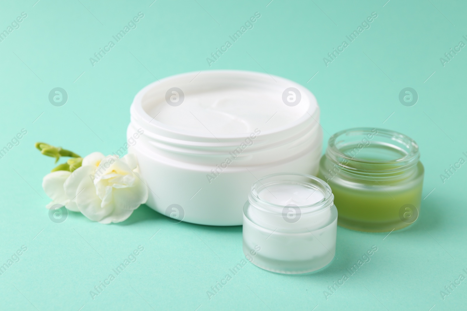 Photo of Moisturizing cream in open jars and freesia flower on turquoise background. Body care product