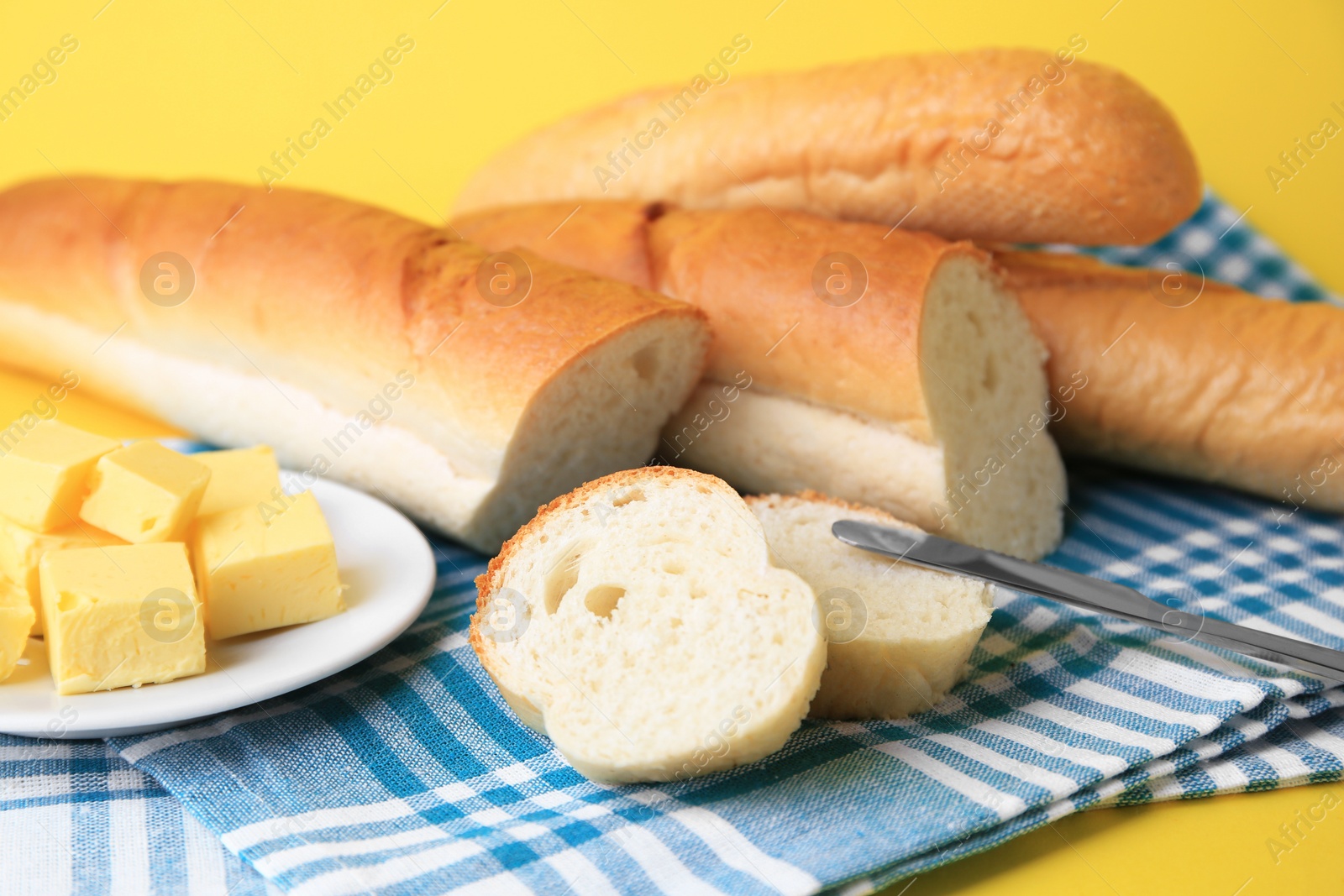 Photo of Whole and cut baguettes with fresh butter on yellow background, closeup