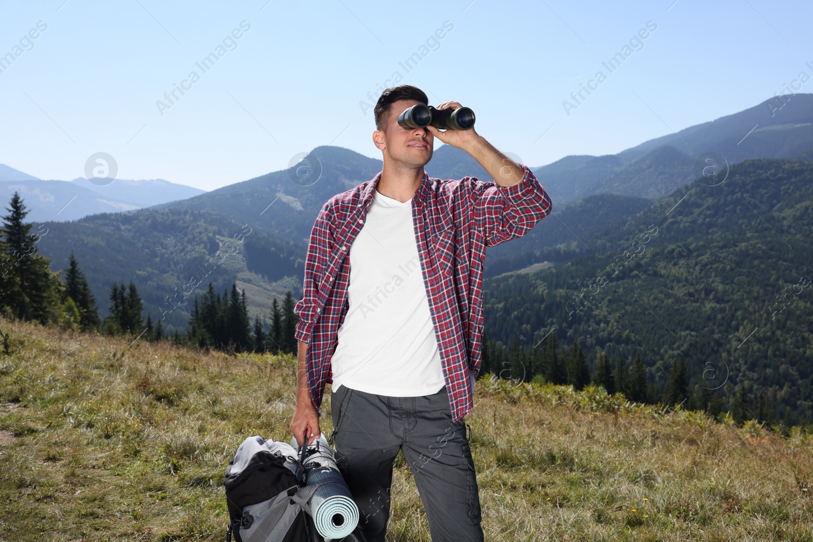 Photo of Tourist with hiking equipment looking through binoculars in mountains