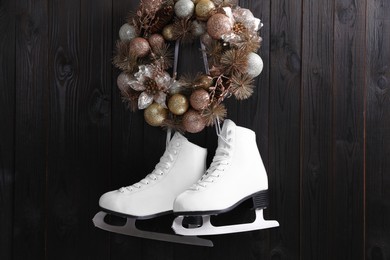 Photo of Pair of ice skates and beautiful Christmas wreath hanging on dark wooden wall