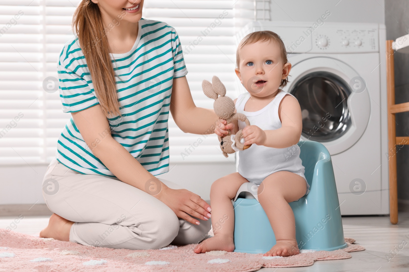 Photo of Mother training her child to sit on baby potty indoors