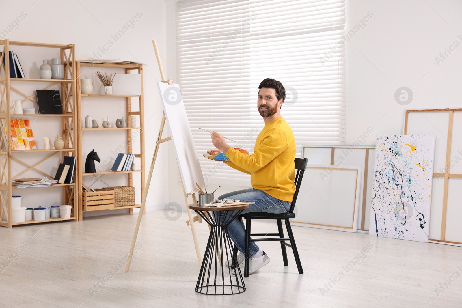 Photo of Happy man painting in studio. Using easel to hold canvas