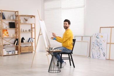 Photo of Happy man painting in studio. Using easel to hold canvas