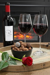 Photo of Red wine, chocolate truffles and rose flower on table against fireplace