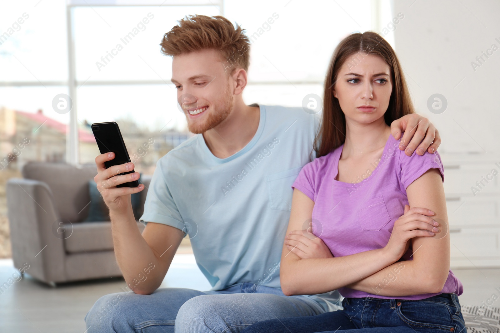 Photo of Young man engaged in smartphone while spending time with his girlfriend at home. Loneliness concept