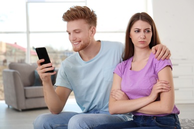 Photo of Young man engaged in smartphone while spending time with his girlfriend at home. Loneliness concept