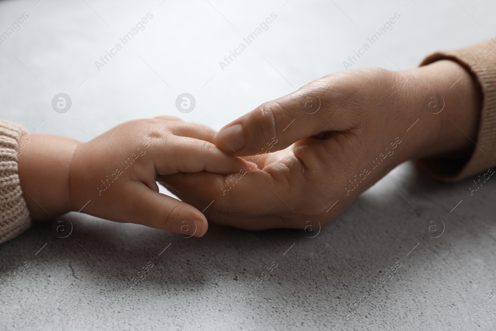 Photo of Woman holding hands with her little daughter at light grey table, closeup