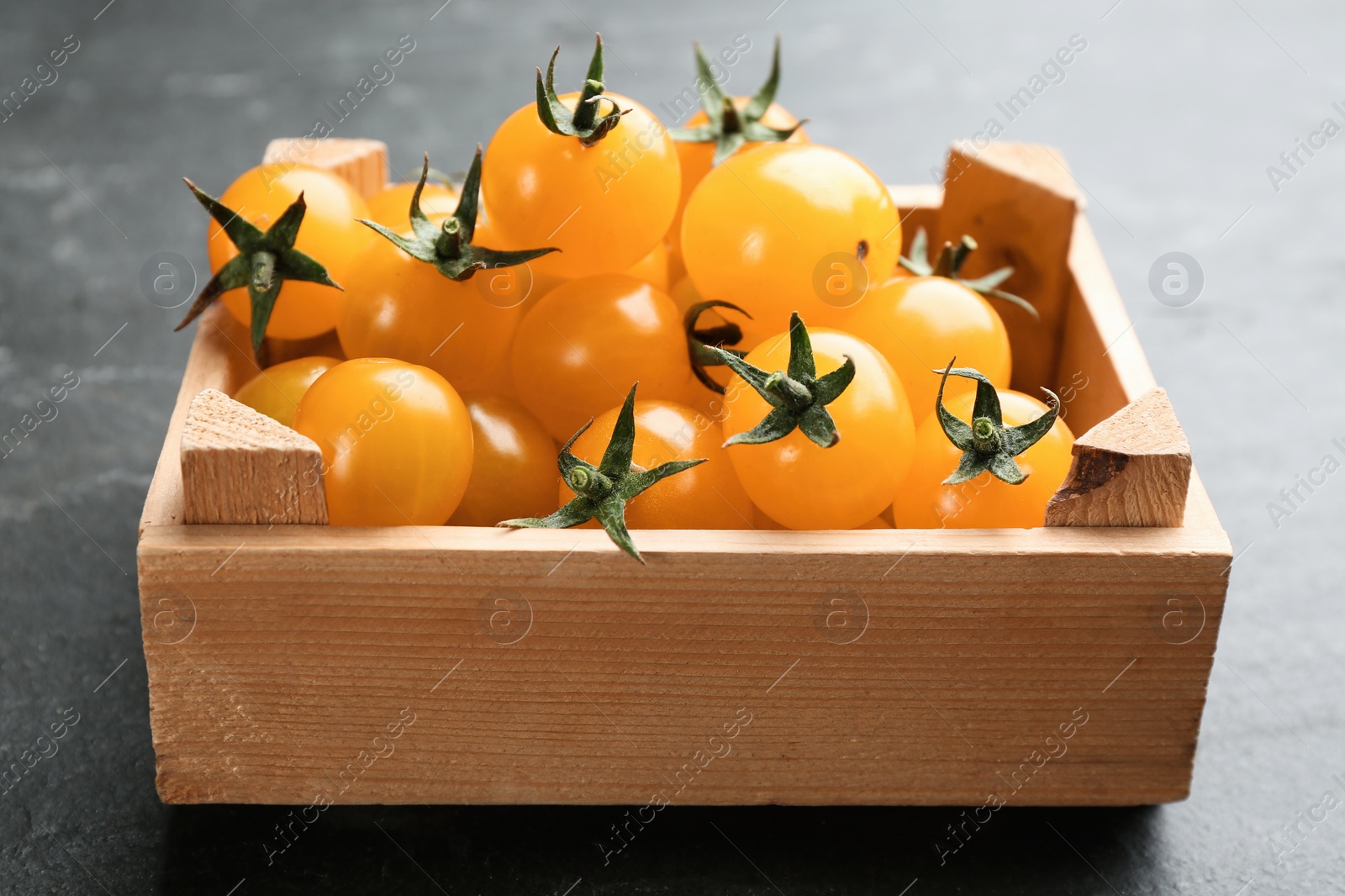 Photo of Ripe yellow tomatoes in wooden crate on black table