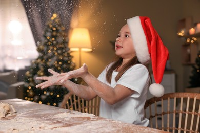Photo of Cute little girl having fun while making dough for Christmas cookies in kitchen