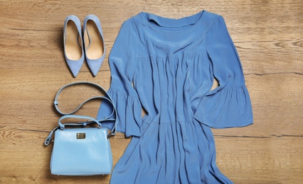 Stylish light blue dress, shoes and bag on wooden background, flat lay