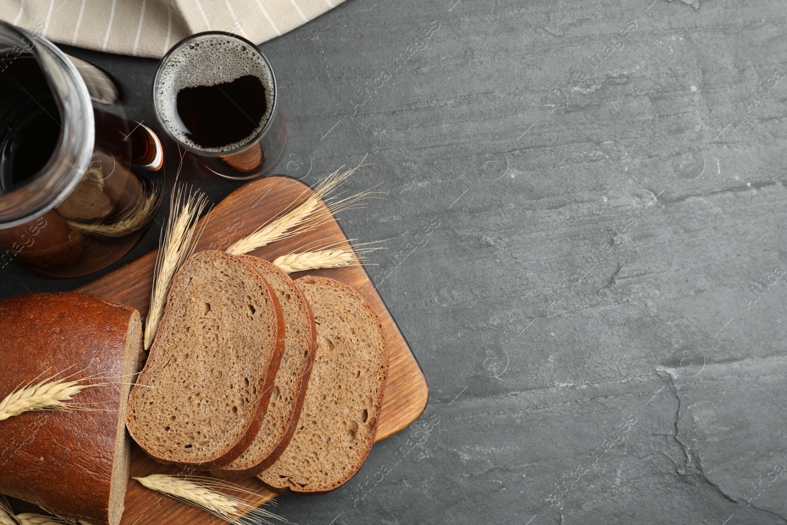 Photo of Delicious kvass, bread and spikes on black slate table, flat lay. Space for text