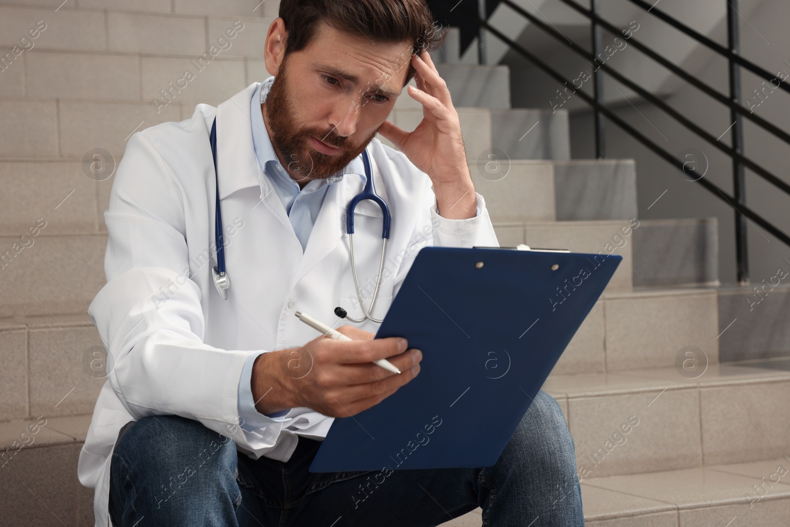 Photo of Upset doctor with clipboard sitting on stairs in hospital
