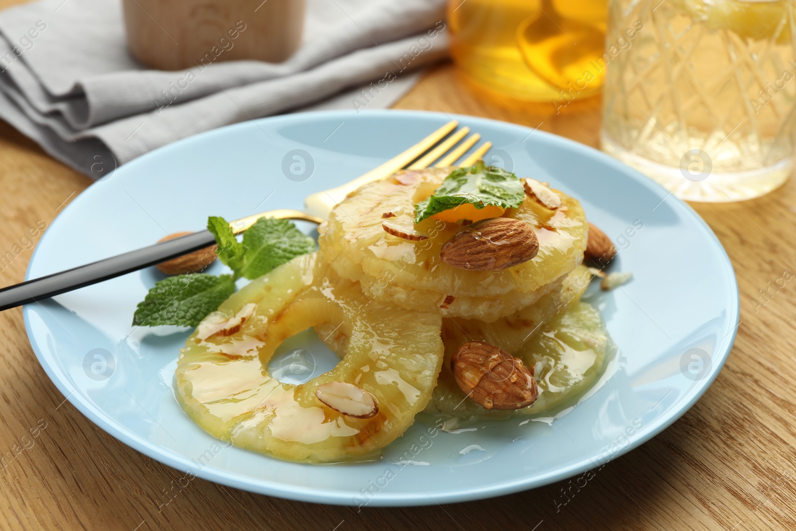 Photo of Tasty grilled pineapple slices served with mint and almonds on wooden table, closeup