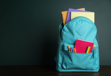 Backpack with different school stationery on wooden table near chalkboard, space for text