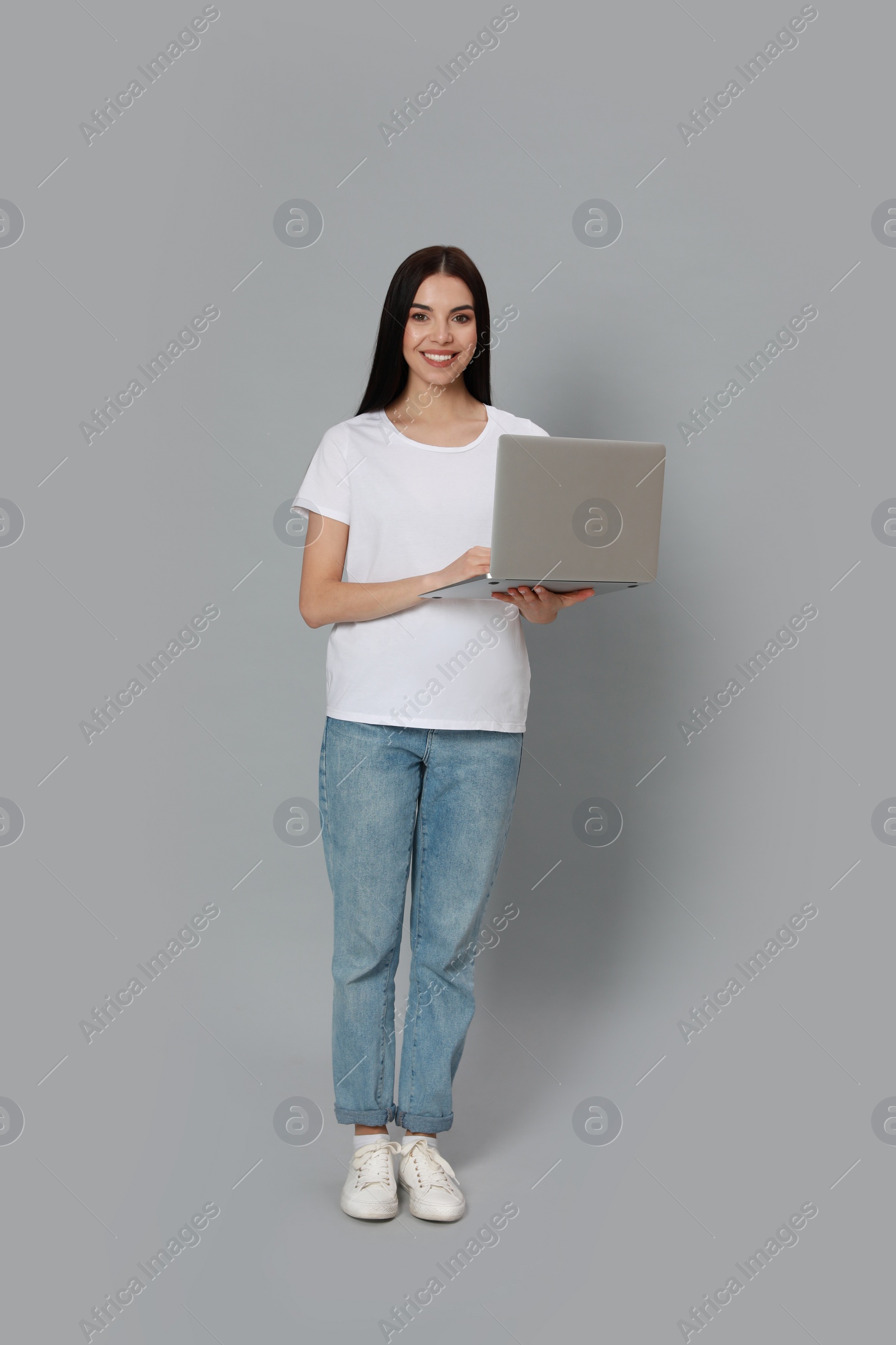 Photo of Young woman with modern laptop on light grey background