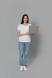 Young woman with modern laptop on light grey background