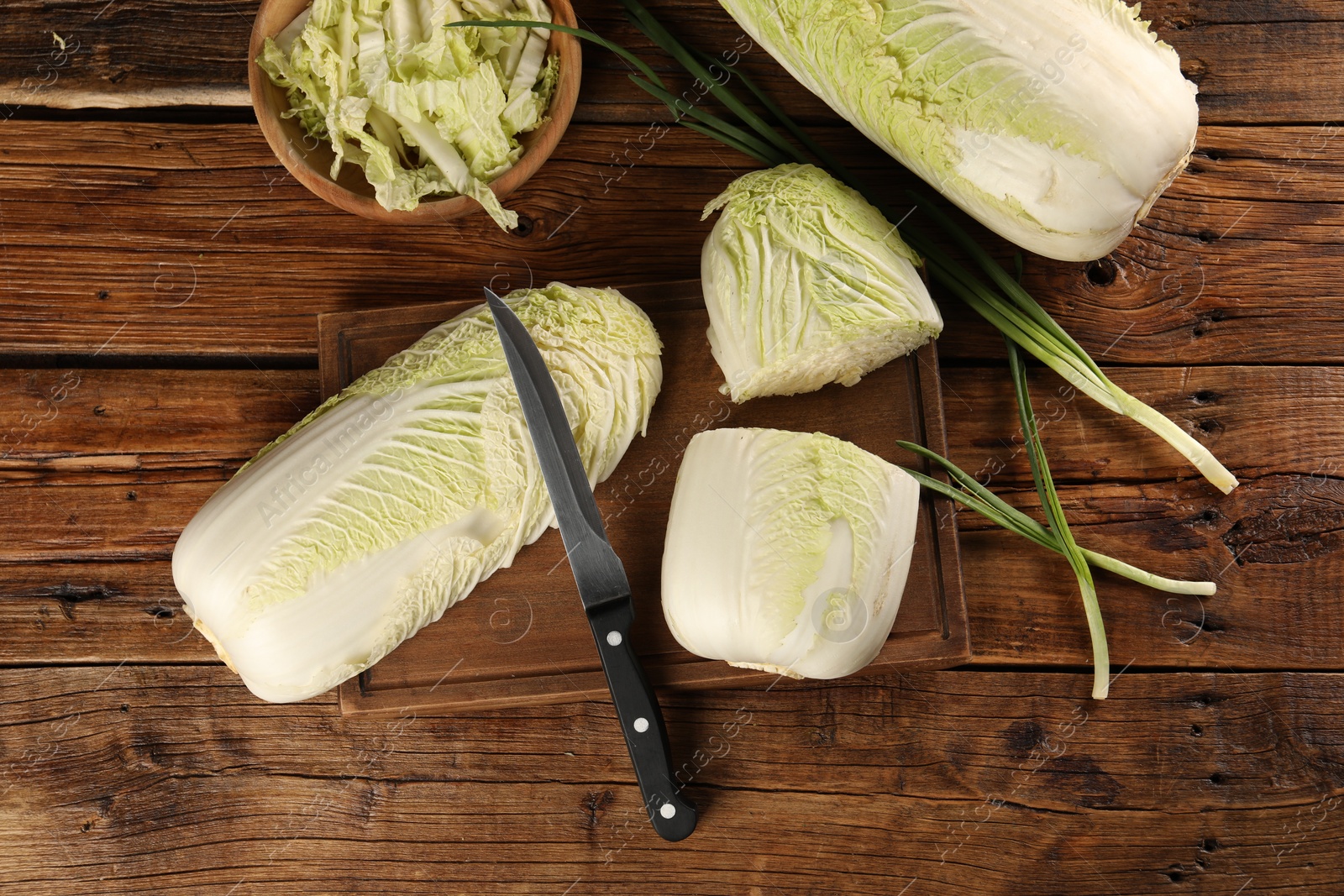 Photo of Fresh Chinese cabbages, green onion and knife on wooden table, flat lay