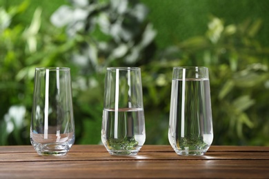 Photo of Empty, half and full glasses of water on wooden table against blurred background