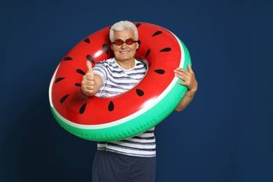 Photo of Funny mature man with bright inflatable ring on dark blue background