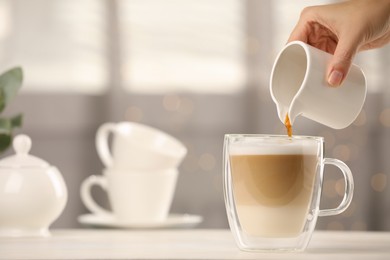 Photo of Woman pouring coffee into cup with milk at table indoors, closeup