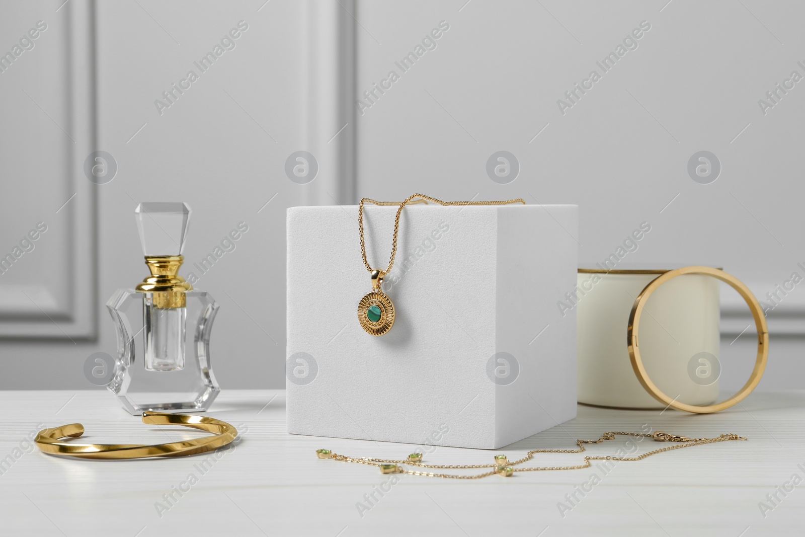 Photo of Stylish presentation of bijouterie on podiums and perfume bottle on white wooden table