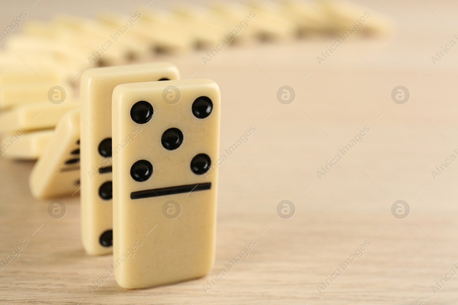 Photo of White domino tiles falling on wooden table, closeup. Space for text
