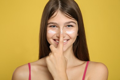 Photo of Teenage girl applying sun protection cream on her face against yellow background