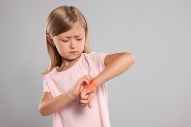 Suffering from allergy. Little girl scratching her hand on light gray background, space for text