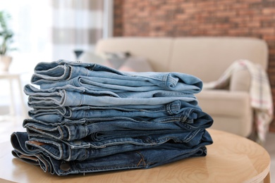 Photo of Stack of stylish jeans on table against blurred background