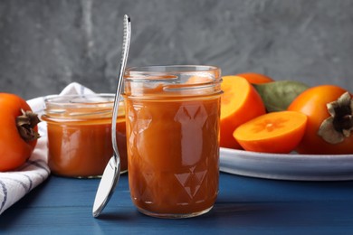 Photo of Delicious persimmon jam in glass jar served on blue wooden table