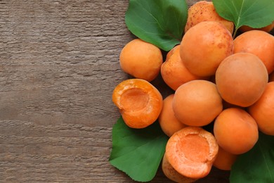 Delicious ripe apricots with green leaves on wooden table, top view. Space for text