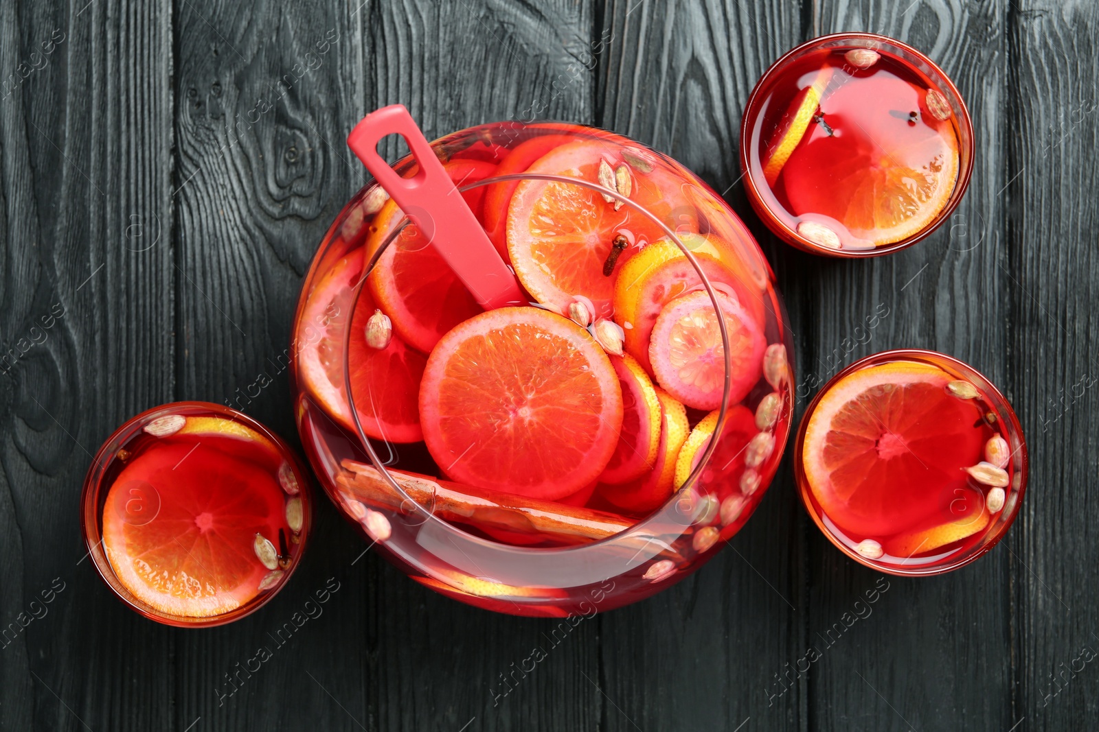 Photo of Bowl and glasses of delicious aromatic punch drink on black wooden table, flat lay