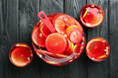 Photo of Bowl and glasses of delicious aromatic punch drink on black wooden table, flat lay