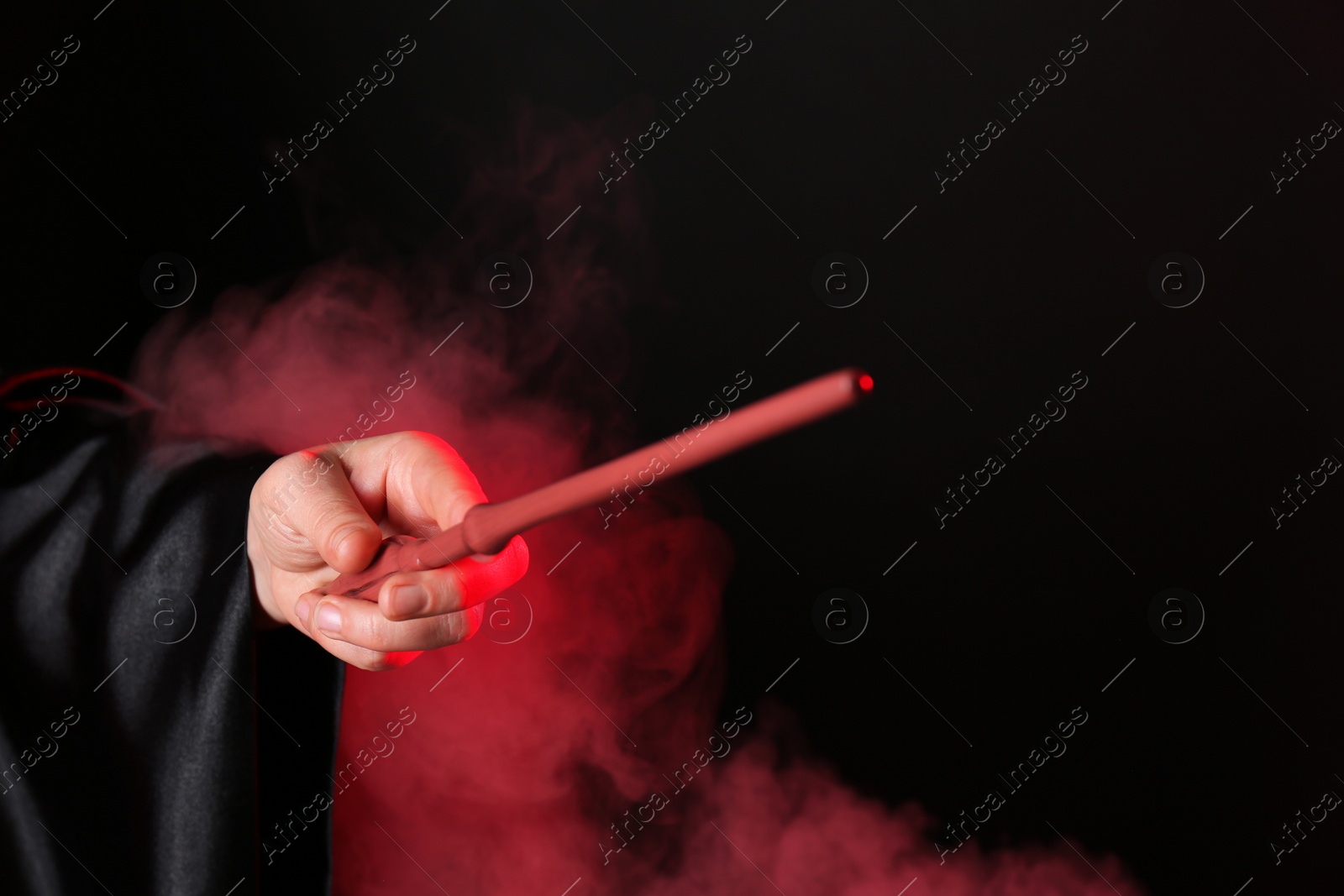 Photo of Magician holding wand in smoke on dark background, closeup. Space for text