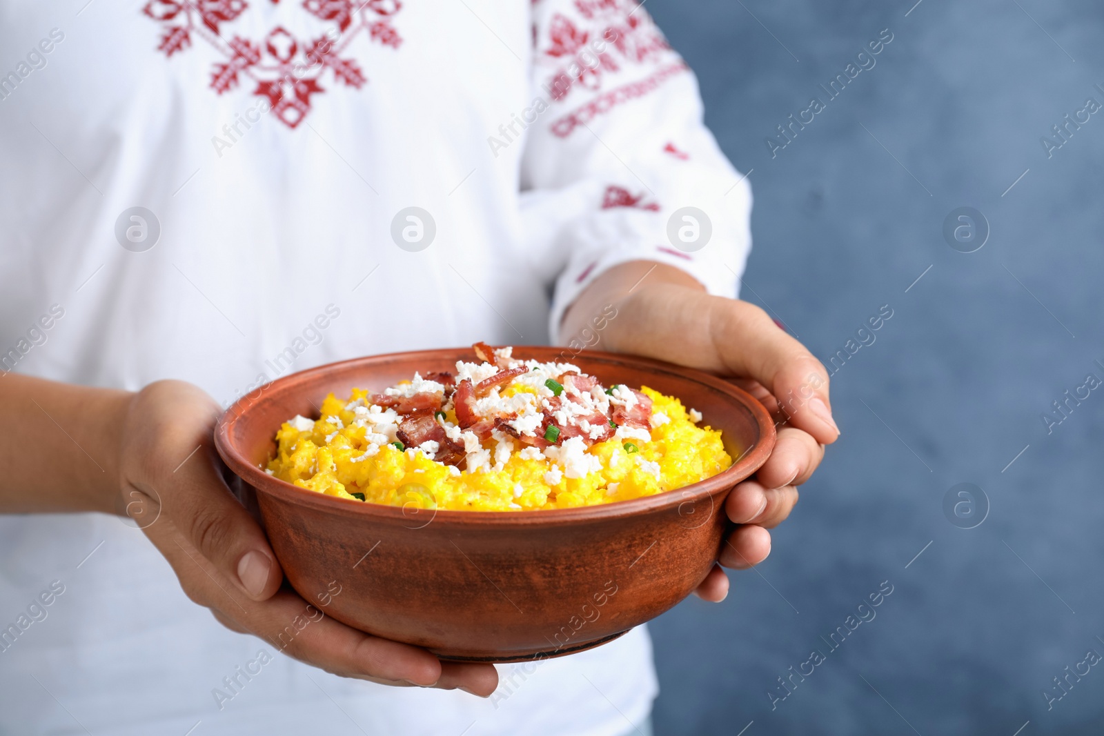 Photo of Woman holding bowl of banosh with brynza and pork cracklings on blue background, closeup. Traditional Ukrainian dish