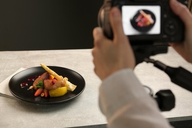 Woman taking picture of dish with chicken, parsnip and strawberries on grey table in professional photo studio, closeup. Food stylist