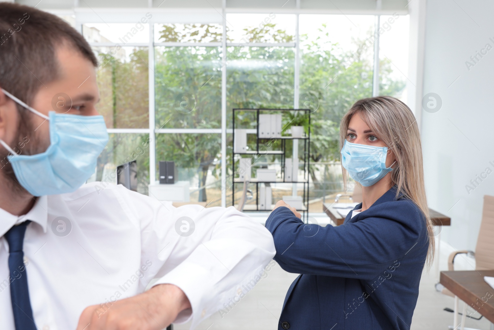 Photo of Office employees in masks greeting each other by bumping elbows at workplace