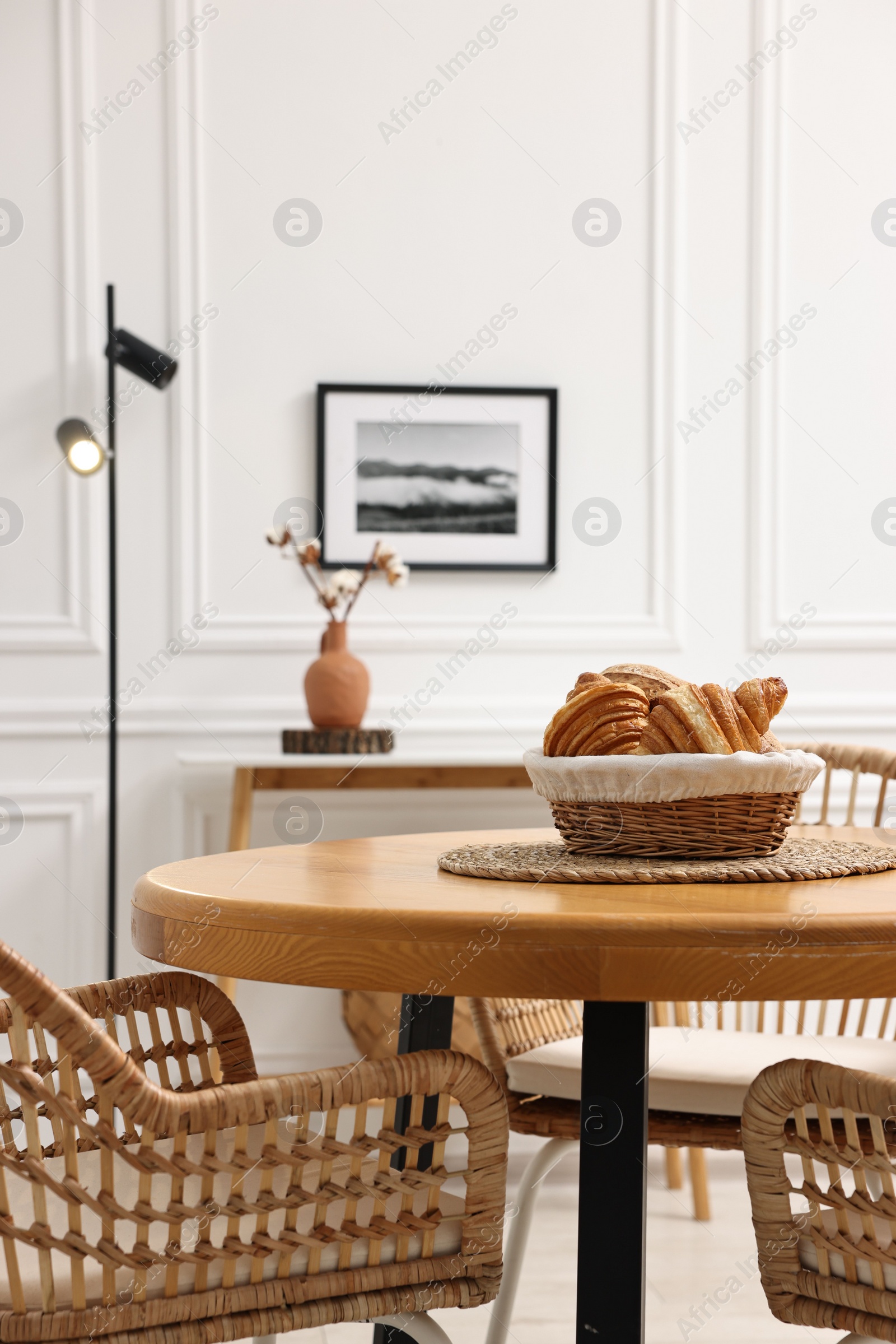 Photo of Tasty croissants on table and wicker chairs in dining room. Interior design