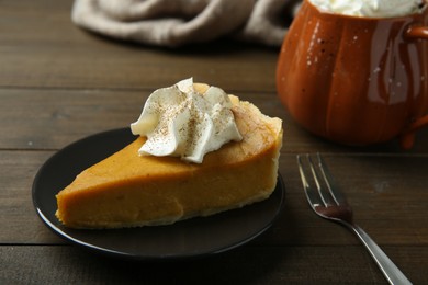 Piece of delicious pumpkin pie with whipped cream and fork on wooden table, closeup