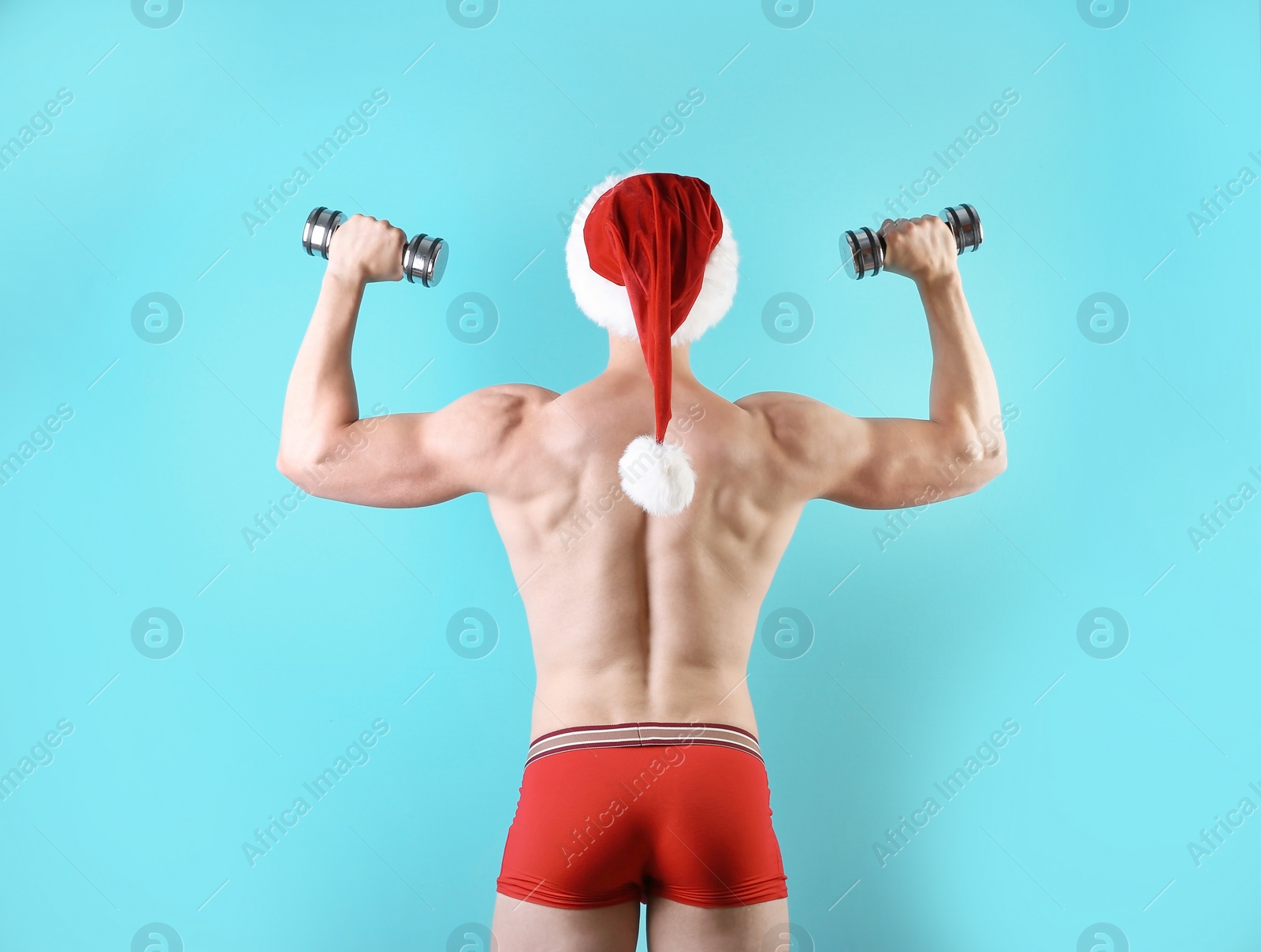 Photo of Young muscular man in Santa hat with dumbbells on color background