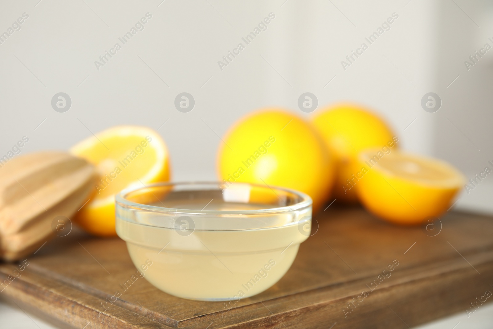 Photo of Freshly squeezed lemon juice in bowl on wooden board, closeup