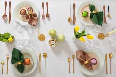 Festive Easter table setting with painted eggs, burning candles and yellow tulips, flat lay