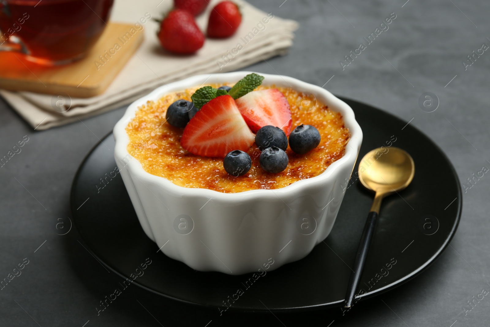 Photo of Delicious creme brulee with berries and mint in bowl on grey table, closeup