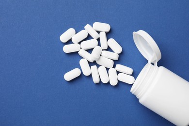 Photo of Vitamin pills and bottle on blue background, top view