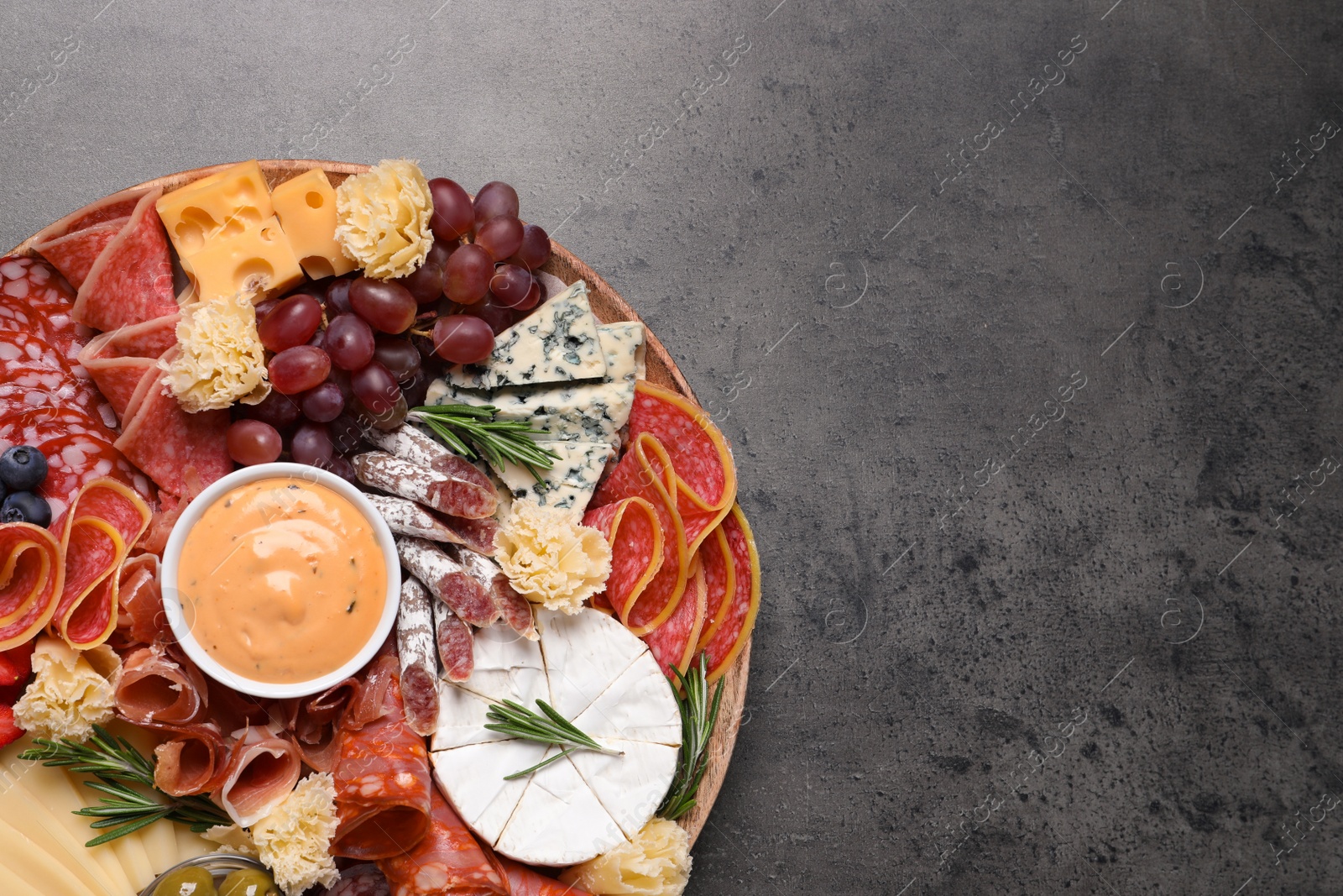 Photo of Wooden plate with different delicious snacks on grey table, top view. Space for text