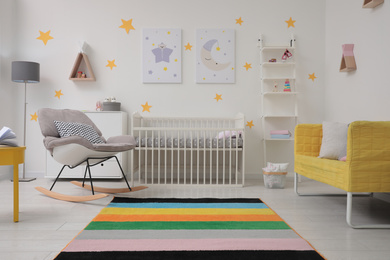 Stylish baby room interior with crib, rocking chair and sofa