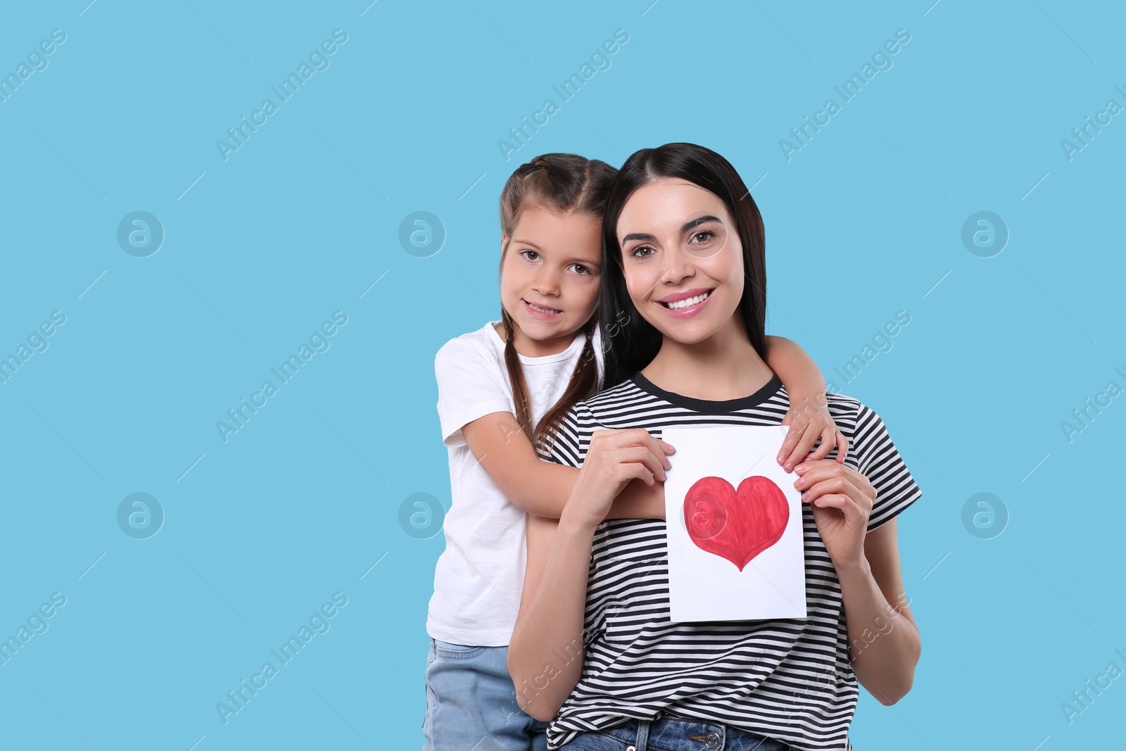 Photo of Happy woman with her cute daughter and handmade greeting card on light blue background, space for text. Mother's day celebration